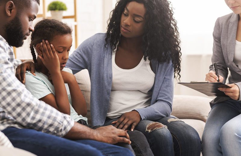 Black parents with young daughter in therapy session - family and recovery