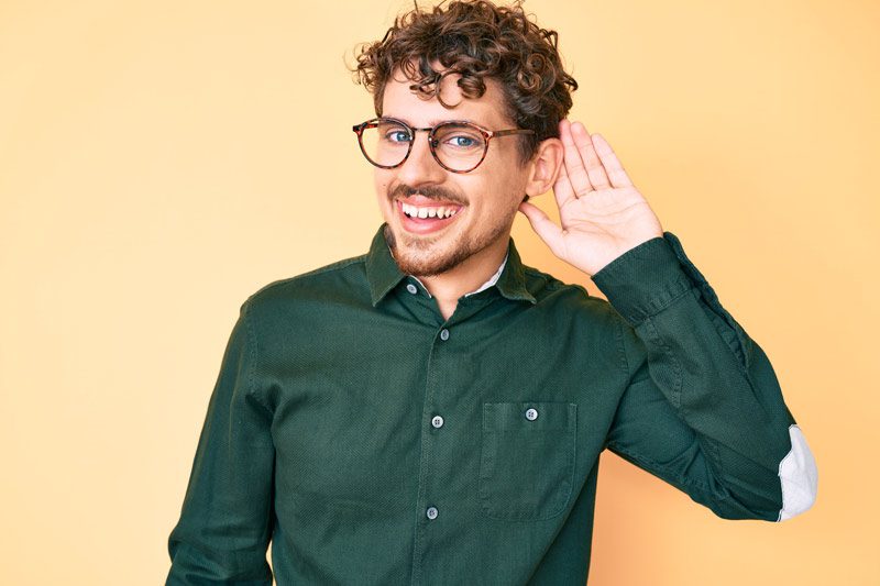 smiling man in glasses holding his hand up to his ear in a listening gesture - recovery podcasts