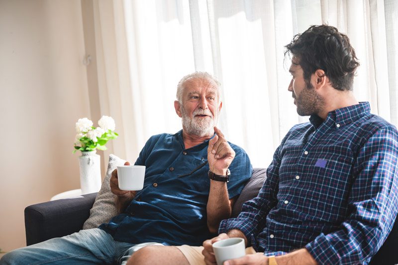 senior father and adult son having a talk on sofa and drinking coffee - adult child