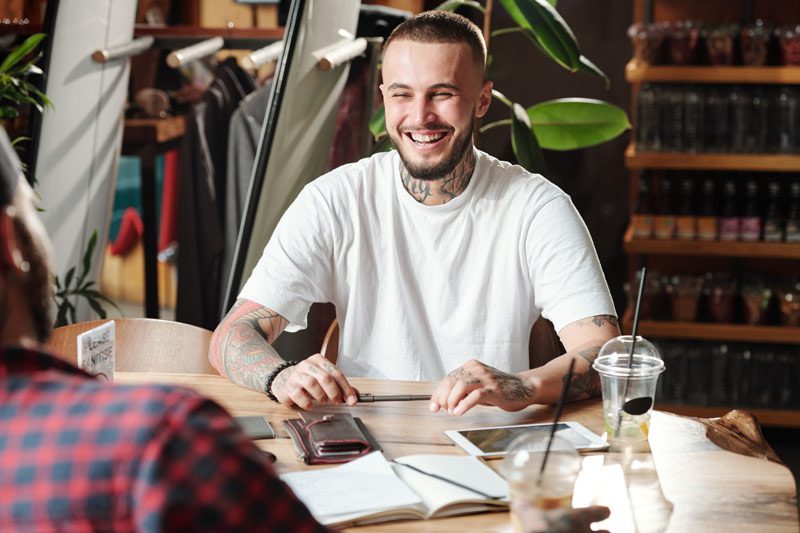 handsome tattooed young man sitting a table with his friends laughing - laughter