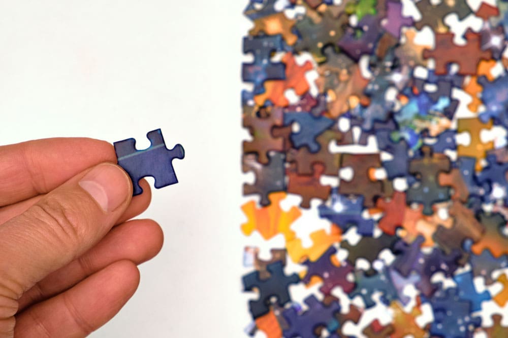 hand holding a puzzle piece over a lot of puzzle pieces